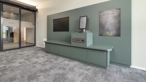 Un área de recepción moderna con alfombra gris, una puerta de cristal que da a otra habitación y un panel de exhibición en la pared.