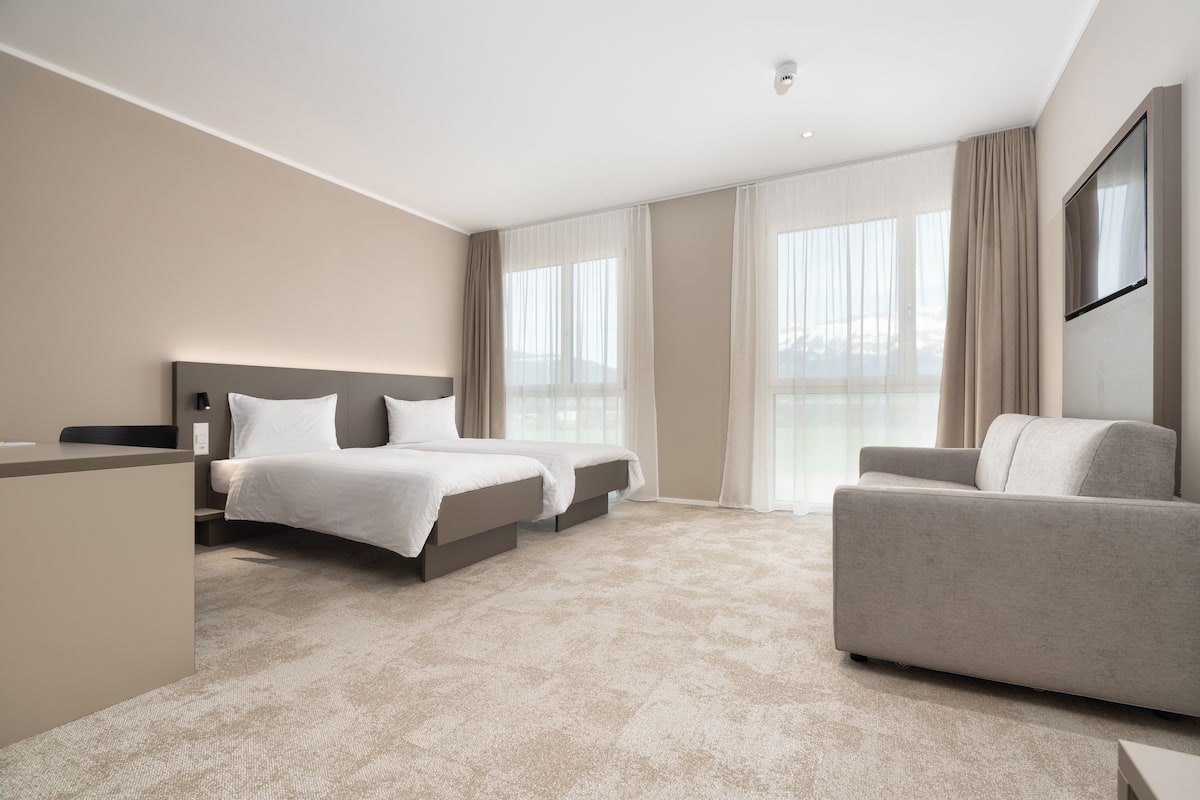 A modern hotel room with a large bed, a sofa, and a desk.