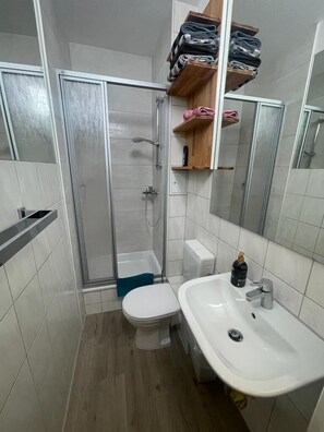 Een kleine badkamer met douche, toilet en wastafel.