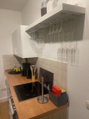 Een keuken met een zwarte kookplaat, een koffiezetapparaat en een rekje met kruiden.