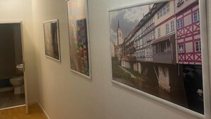 A hallway with three framed pictures on the wall, a wooden floor, and a door leading to a bathroom.