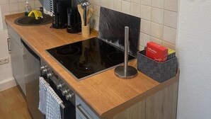 A compact kitchen with a black induction cooktop, a coffee maker, and a wine rack.