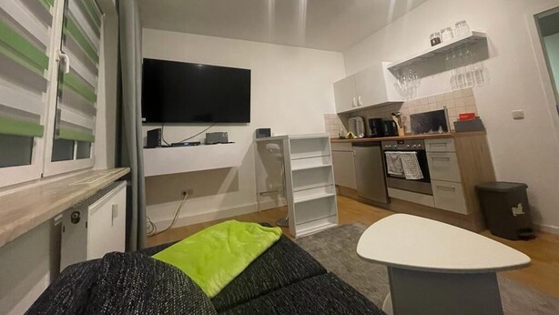 A compact living space with a kitchenette, a flat-screen TV mounted on the wall, and a dining area with a table and chairs.
