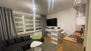 A modern living room with a sofa, a coffee table, and a TV. There is a kitchen area with a counter and cabinets.