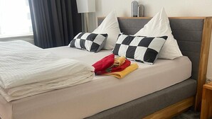 A neatly made bed with checkered pillows, a folded red towel, and a grey headboard.