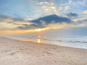 Ein Strand mit Sonnenuntergang, Sandküste und Meereswellen.