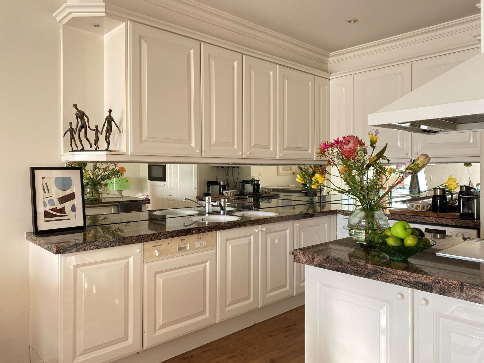 A modern kitchen with white cabinetry, granite countertops, and a stainless steel range hood.
