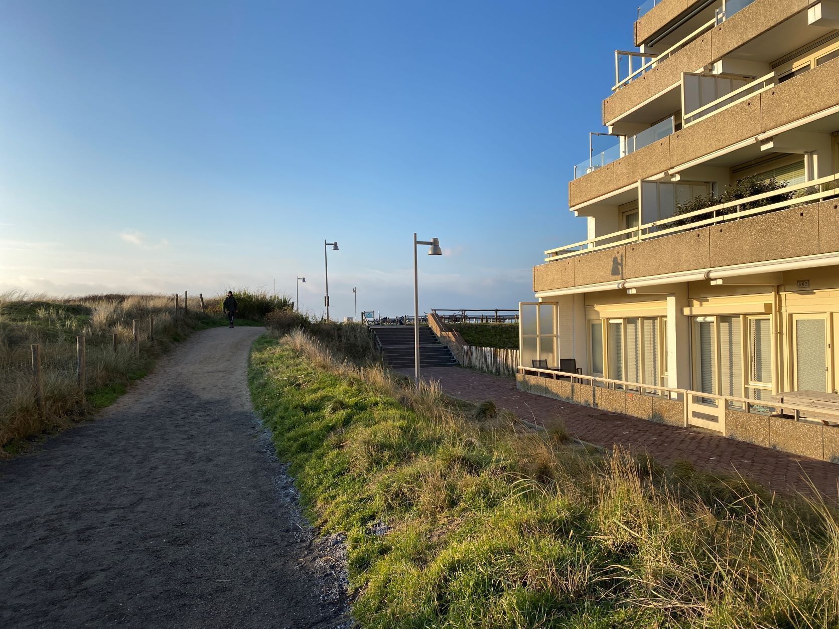 Un sentier côtier mène à un bâtiment moderne doté de nombreux balcons et de grandes fenêtres.