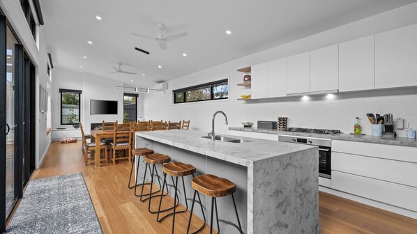 A modern kitchen with a central island, bar stools, and a dining area with wooden chairs.