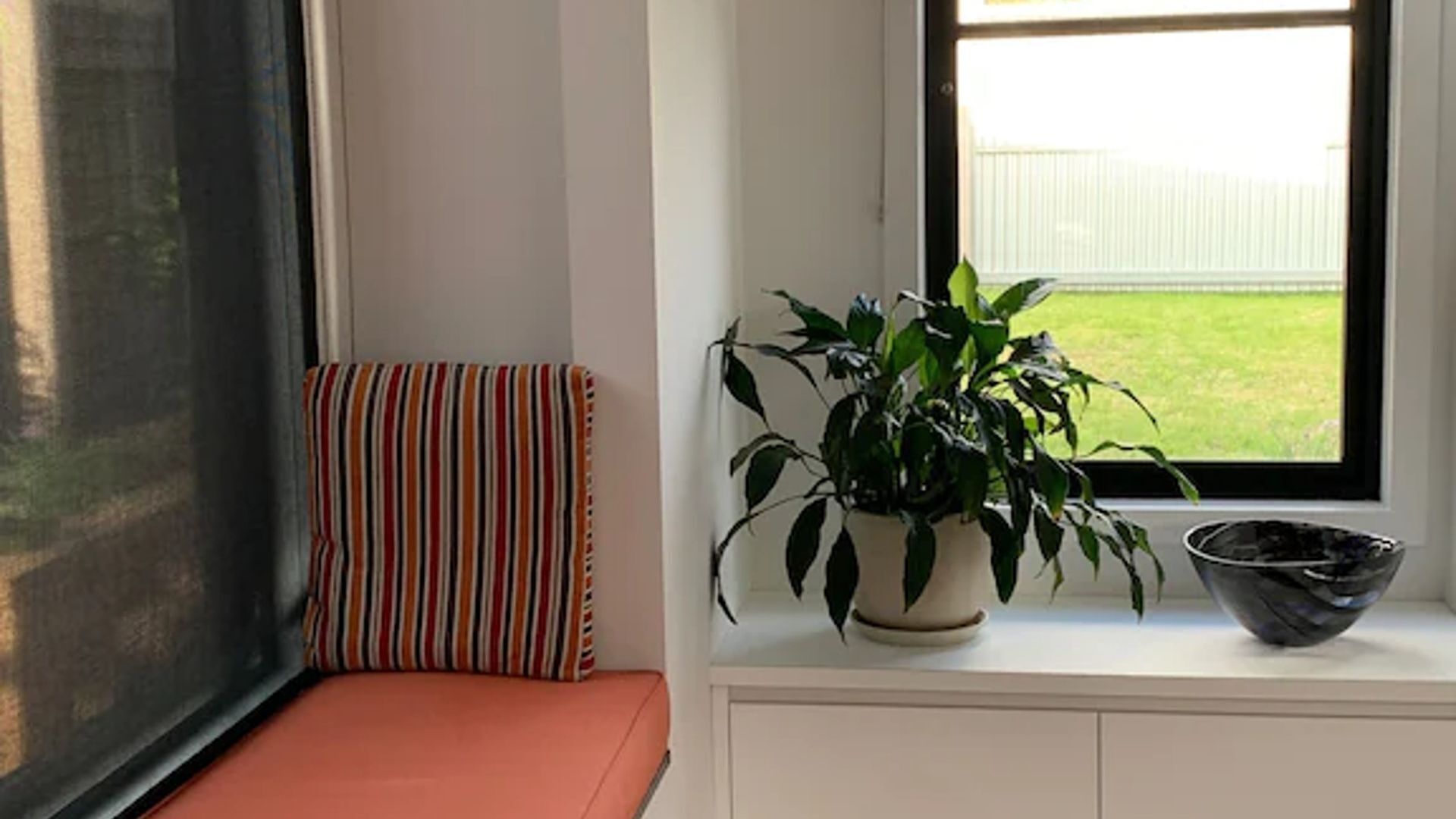 A window seat with a striped cushion, a potted plant, and a bowl on a white cabinet.