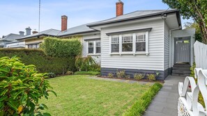 A single-story house with a front yard, a white picket fence, and a visible chimney.