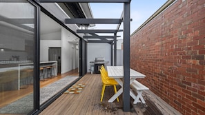 A patio with a table and chairs, a grill, and a brick wall.
