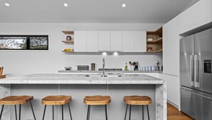A modern kitchen with a marble island, stainless steel appliances, and wooden stools.
