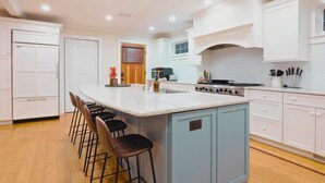 A kitchen with white cabinets, a large island with bar stools, a stove, and a sink.