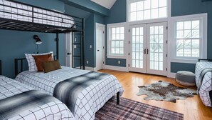 A bedroom with a bunk bed, a desk, and a large window with a view.