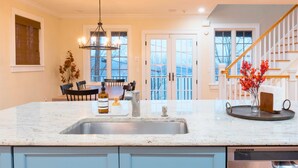 A kitchen with a large island, a dining area with chairs, a chandelier, and a staircase.