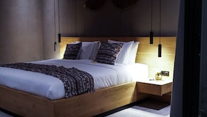 A modern bedroom with a wooden bed frame, white bedding, patterned pillows, and a bedside table with a lamp. - Villa with sunset sea view and jacuzzi - 700m from the beach! (Buleleng)