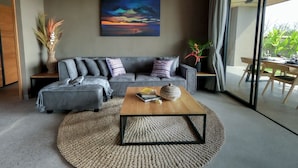 A modern living room with a grey sectional sofa, a wooden coffee table, and a large painting of a sunset. - Villa with sunset sea view and jacuzzi - 700m from the beach! (Buleleng)