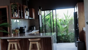 A modern kitchen with a central island, wooden stools, and a view of lush greenery outside. - Villa with sunset sea view and jacuzzi - 700m from the beach! (Buleleng)