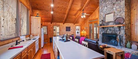 A spacious kitchen with wooden cabinets, a central island, and a stone fireplace.