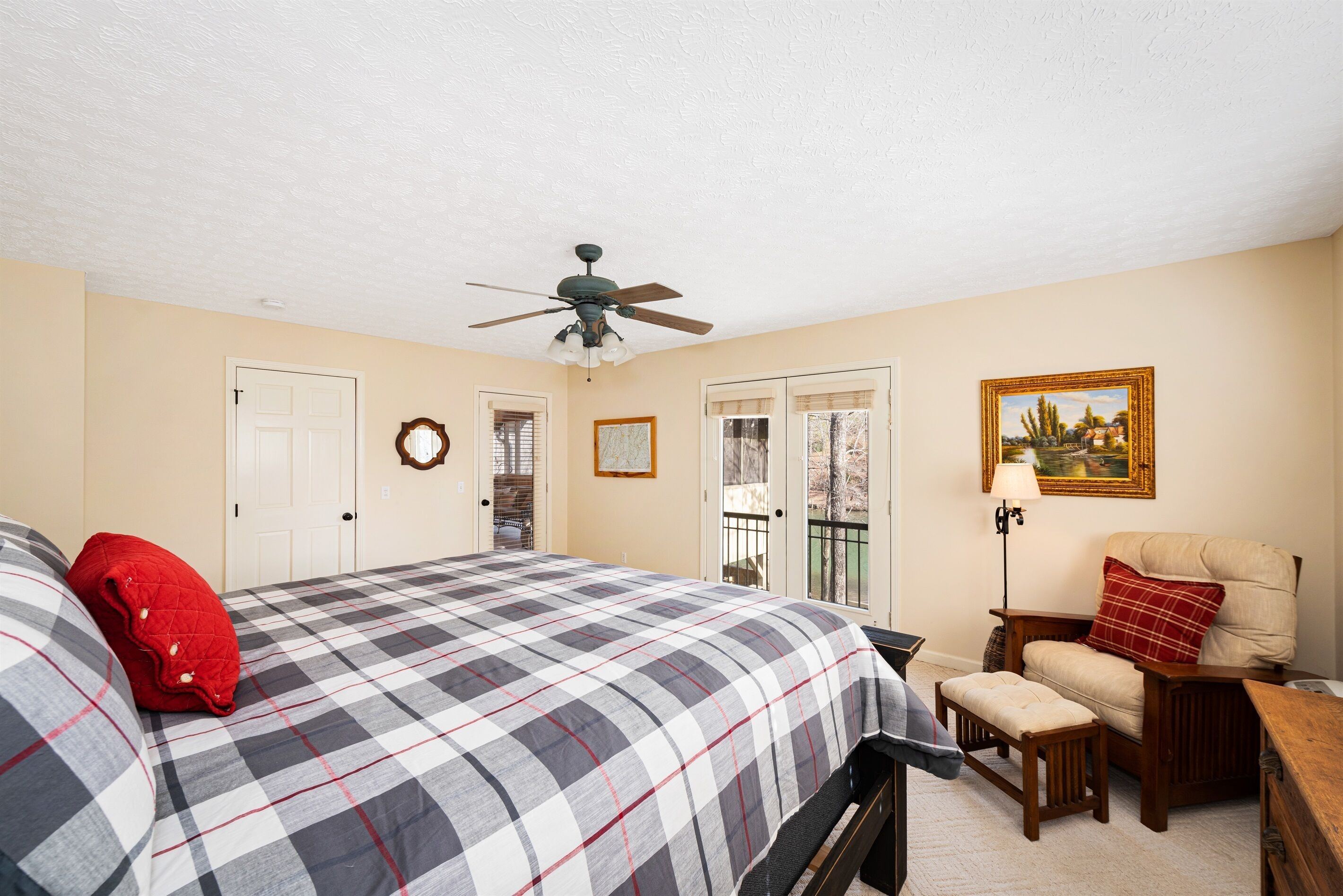 A bedroom with a bed, a chair, a desk, a ceiling fan, and a door.