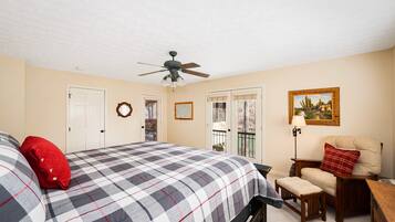 A bedroom with a bed, a chair, a desk, a ceiling fan, and a door.
