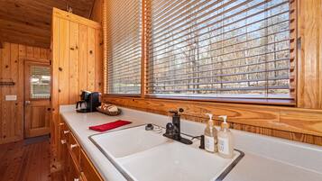 A wooden cabin kitchen with a white sink, black faucet, and wooden cabinets.
