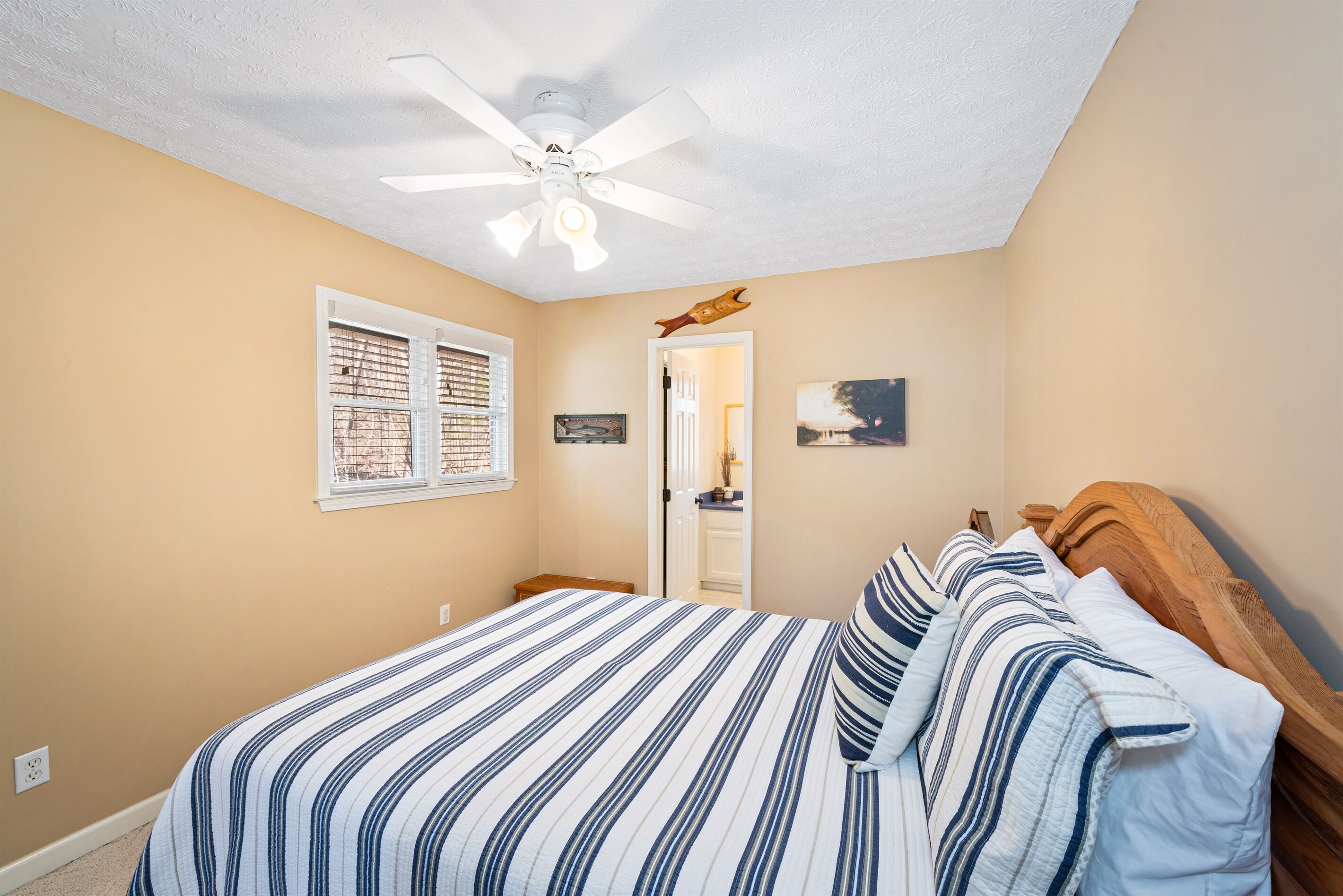 A bedroom with a bed, a ceiling fan, a window with blinds, and a door leading to another room.