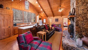 Interior acogedor de una cabaña con paredes de madera, chimenea de piedra, comedor y sala de estar con muebles a cuadros.
