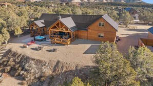 A log cabin with a deck and outdoor seating area, surrounded by a gravel driveway and a mountainous landscape. - Juniper Mountain Retreat |Hot Tub|Game Room| Views (Orderville)