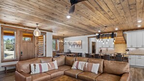 A spacious living room with a large leather sectional sofa, wooden ceiling, and a dining area with a table and chairs. - Juniper Mountain Retreat |Hot Tub|Game Room| Views (Orderville)
