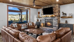 A cozy living room with leather sofas, a stone fireplace, and a large window overlooking a scenic landscape. - Juniper Mountain Retreat |Hot Tub|Game Room| Views (Orderville)