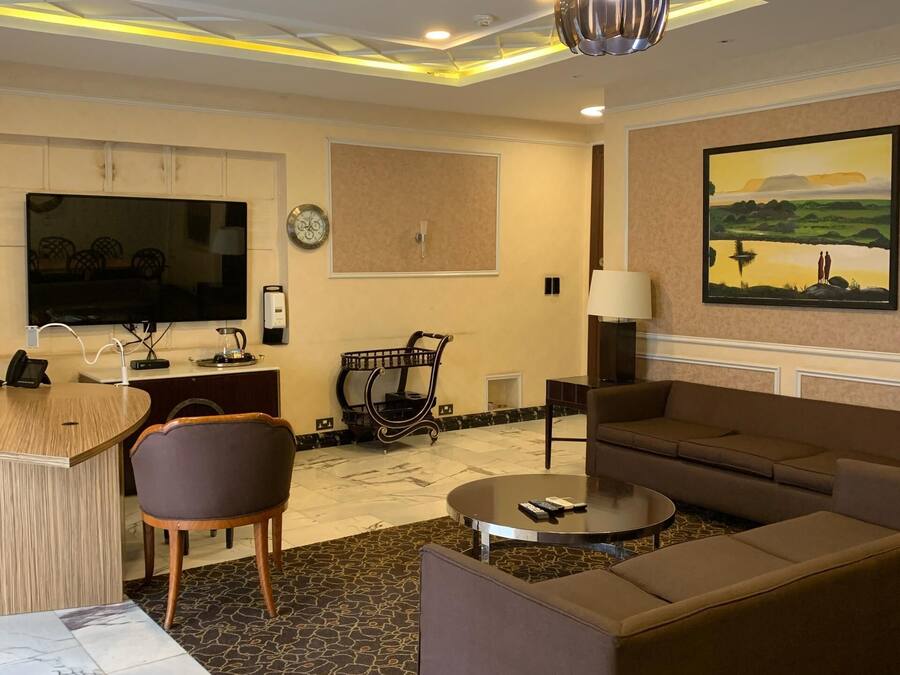 Una sala de estar moderna con un sofá, una mesa de centro y un televisor. Hay un escritorio con una silla, un reloj y un cuadro en la pared.