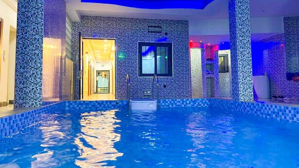 An indoor swimming pool with blue-tiled walls and a ceiling with blue lighting. - BEST PREMIER MAITAMA RESIDENCE (Abuja)