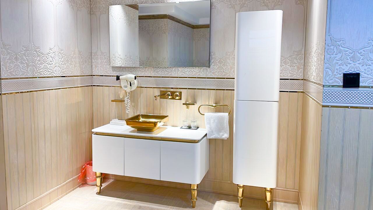A bathroom with a white vanity, gold fixtures, a mirror, and a towel rack.