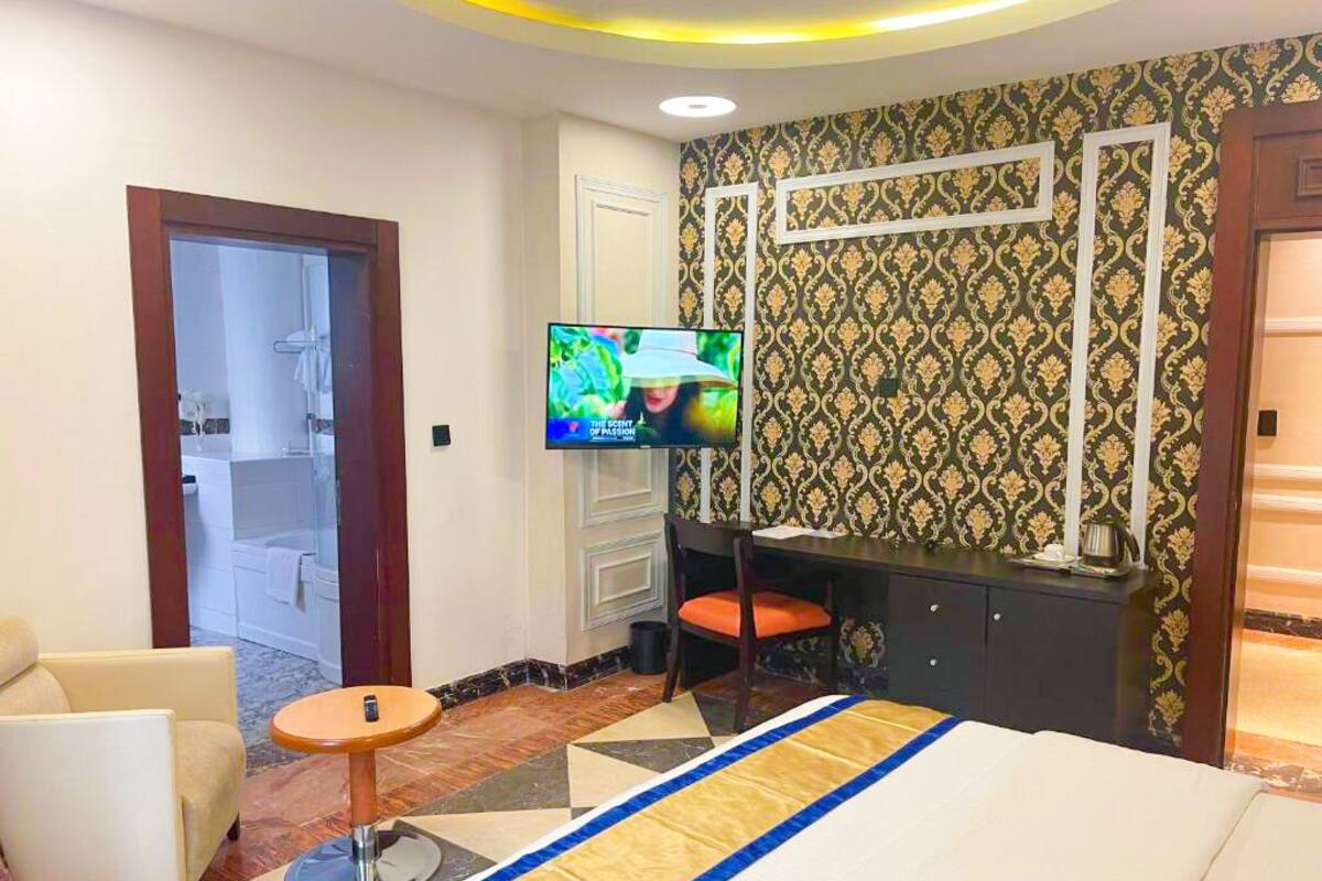 A hotel room with a bed, a desk, a TV, a chair, and a bathroom visible through an open door.