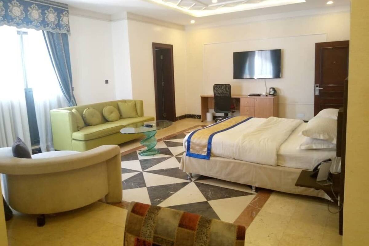 A hotel room with a bed, a sofa, a desk, a TV, and a patterned floor.