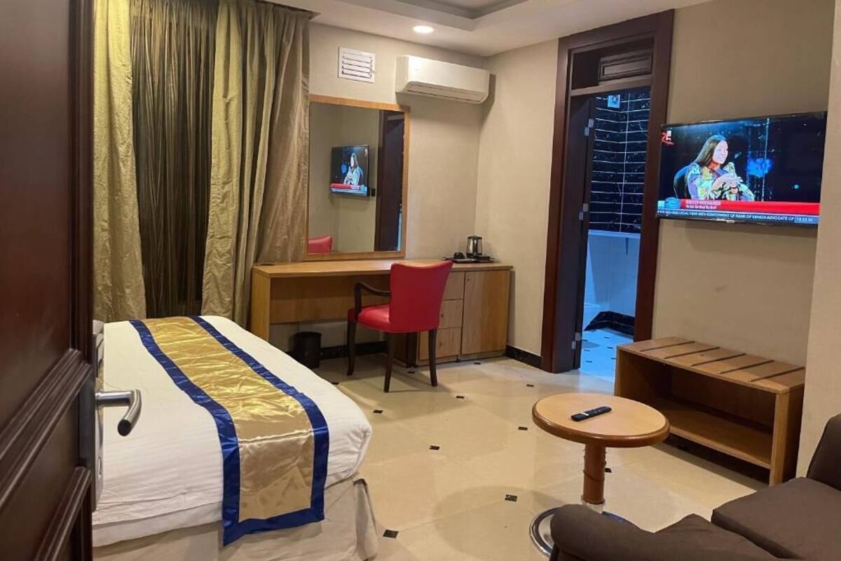 A hotel room with a bed, a desk, a chair, a TV, and a small table.