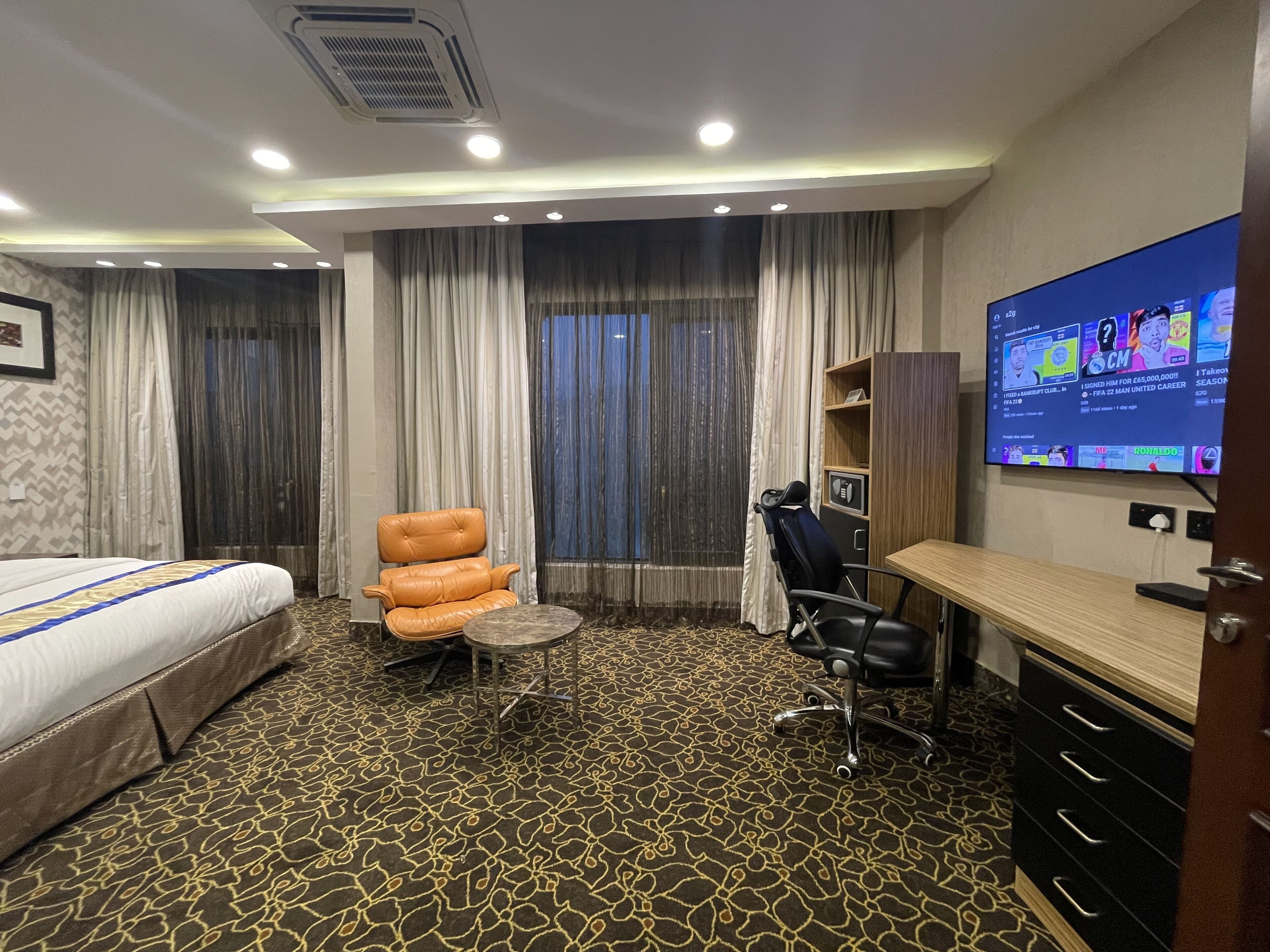 Habitación de hotel con cama, escritorio, silla, televisor y alfombra estampada.