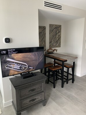 A modern living room with a flat-screen TV, a small wooden table, and a bar stool. - Sea Shells- Ocean/Beach Views for miles. (Myrtle Beach)