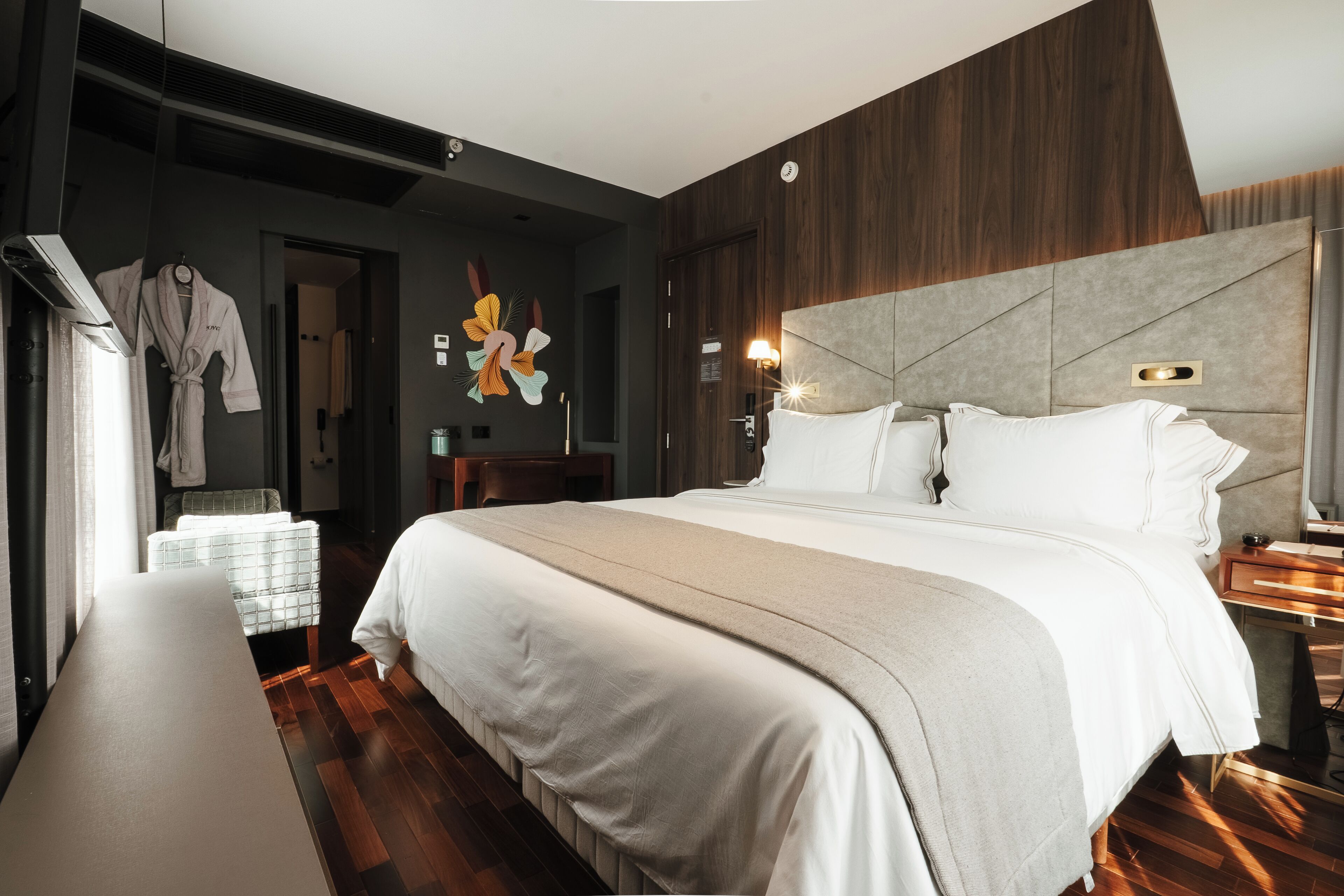 Ein modernes Hotelzimmer mit einem großen Bett, einem Nachttisch, einer Bank und einer Wand-Klimaanlage.