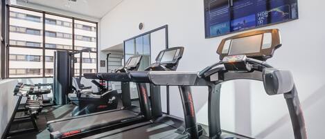 A gym with treadmills, weight machines, and a large window with a view of buildings.