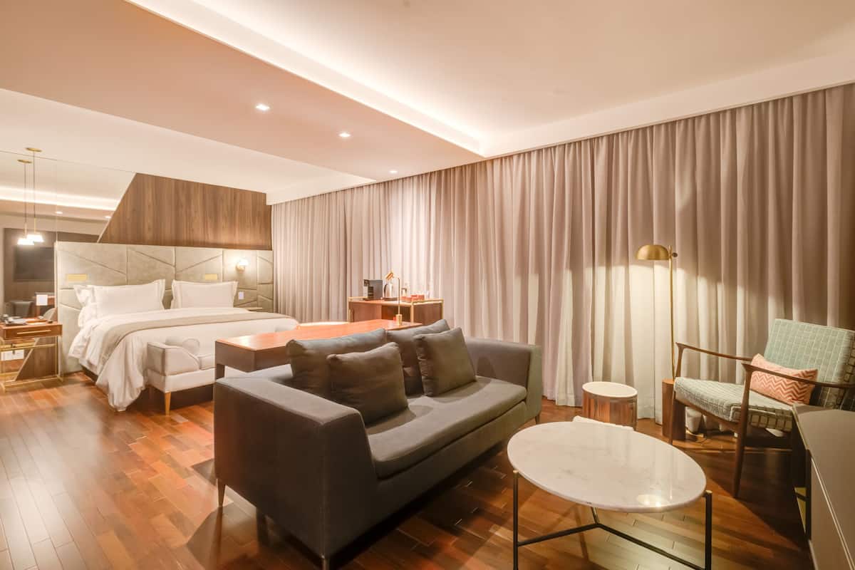 Una habitación de hotel moderna con cama, sofá, sillón y una mesita.