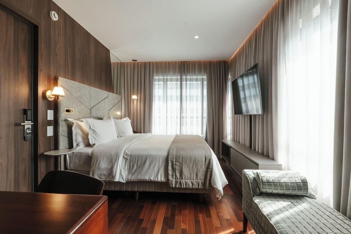 Una habitación de hotel moderna con una cama grande, un escritorio, una silla y un televisor montado en la pared.
