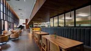 Moderni ravintola, jossa on puupöydät ja -tuolit, baarialue ja suuret ikkunat.