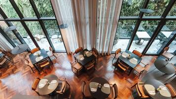 A restaurant with multiple tables and chairs, large windows, and a herringbone floor pattern.