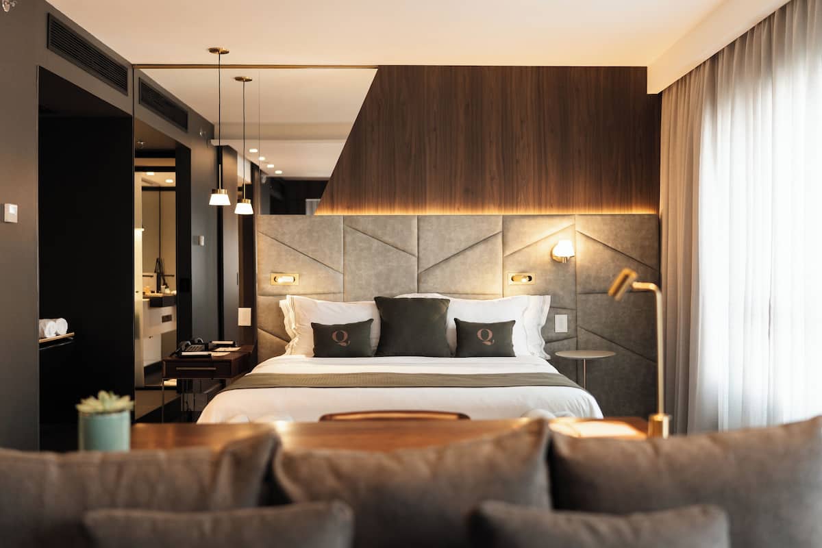 Una habitación de hotel moderna con una cama grande, cabecera con diseños geométricos, mesitas de noche y vistas a la ciudad.