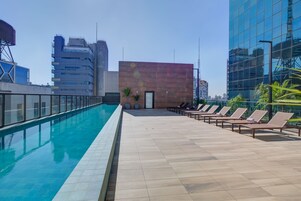 A rooftop pool with lounge chairs and a modern building in the background.