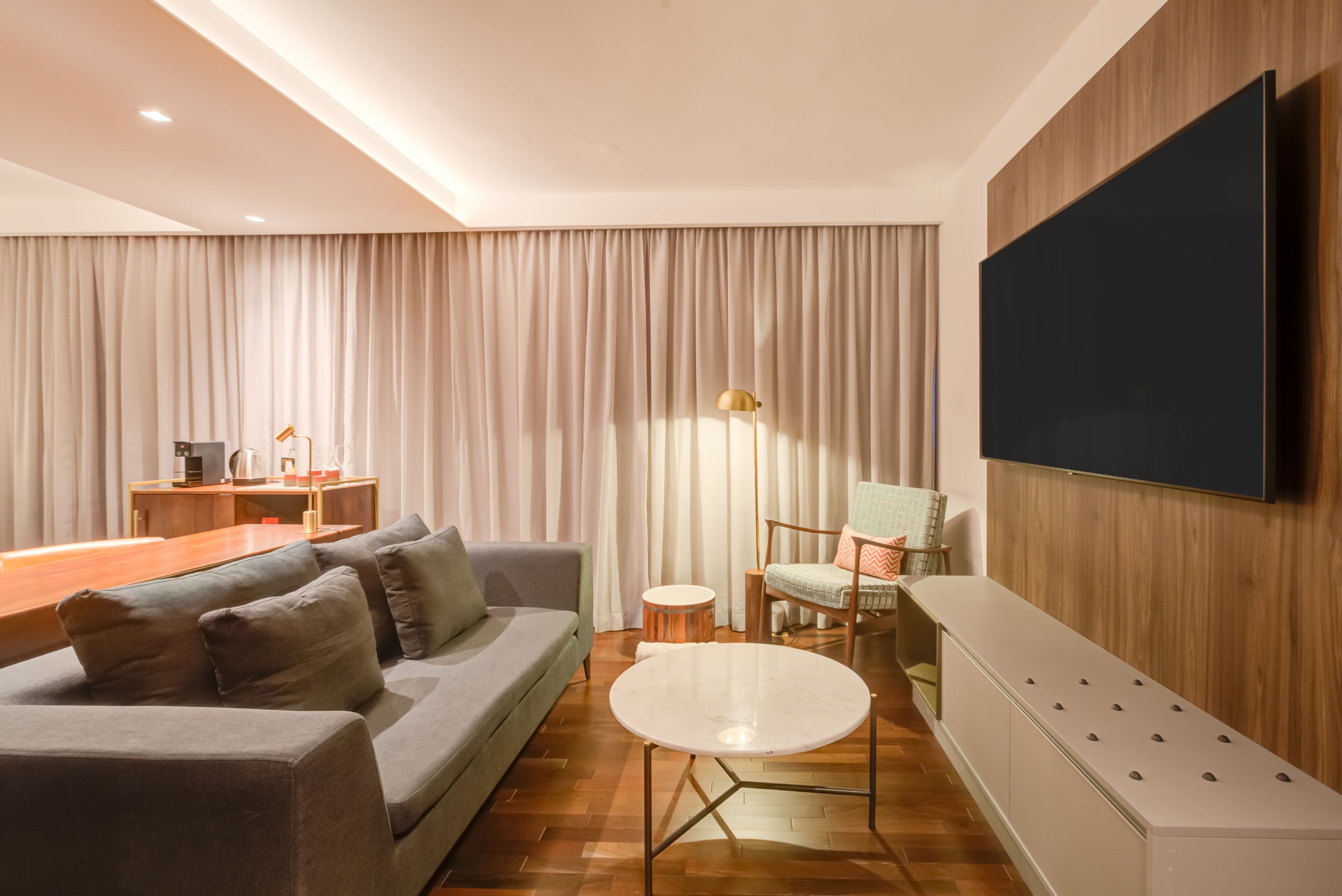Ein modernes Wohnzimmer mit einer Couch, einem runden Couchtisch, einem an der Wand montierten Fernseher und einer Holzkommode.