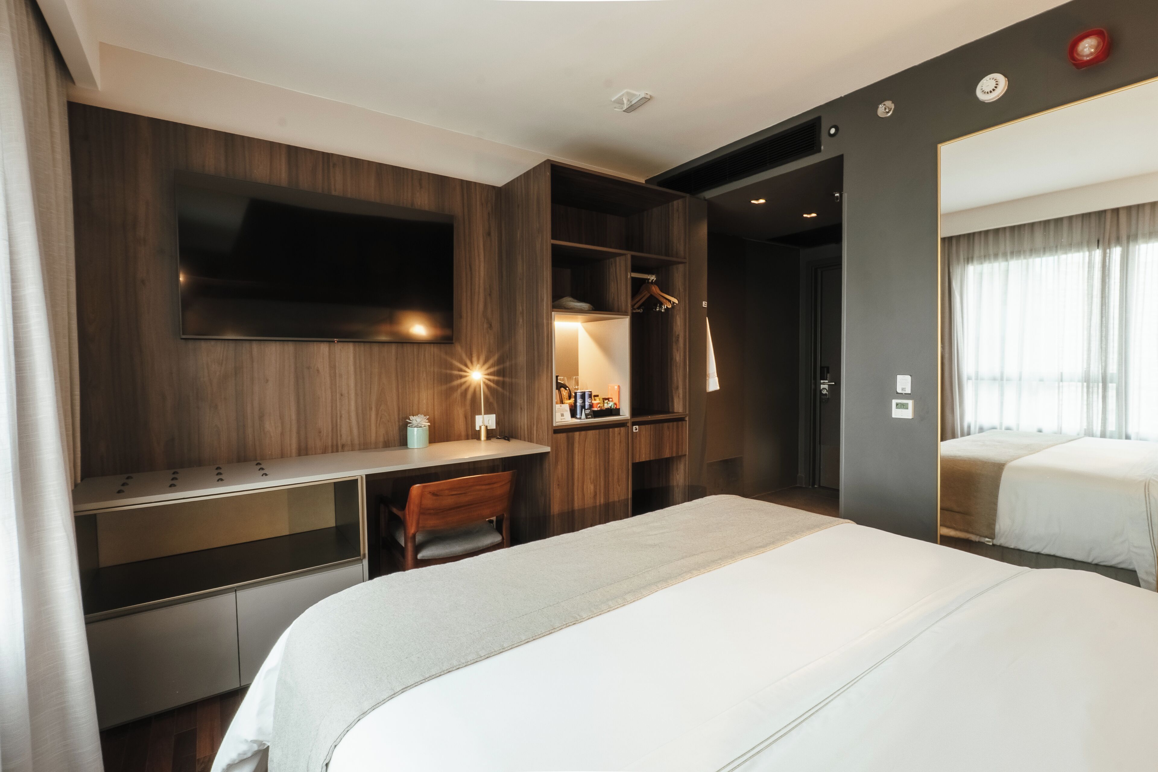 Ein Hotelzimmer mit einem großen Bett, einem Schreibtisch mit Stuhl, einem an der Wand befestigten Fernseher und einem Kleiderschrank.